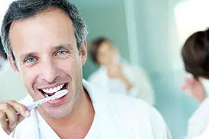 Man and woman brushing their pearly whites and looking in the mirror.