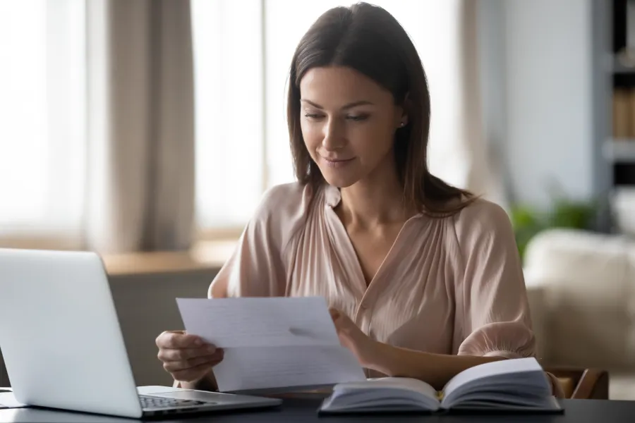 Dark haired woman sitting at her table reviewing her plans benefits.