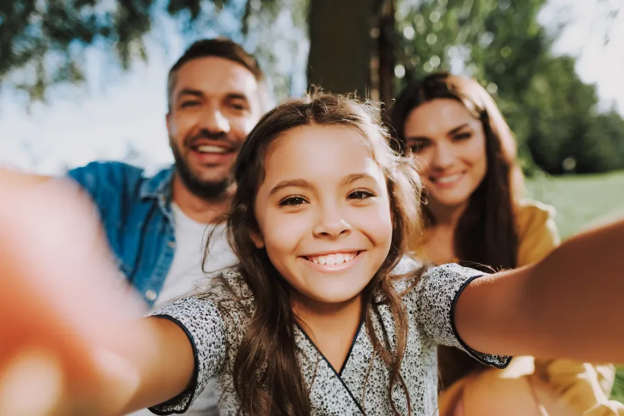 Young girl taking a smiling selfie with her parents.